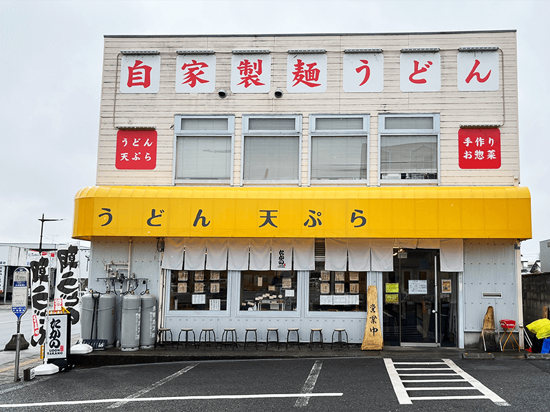 10 台が停められる広い駐車場を備えた「うどん たかの」。「自家製麺うどん」の大きな看板文字と黄色のオーニングテントが目印